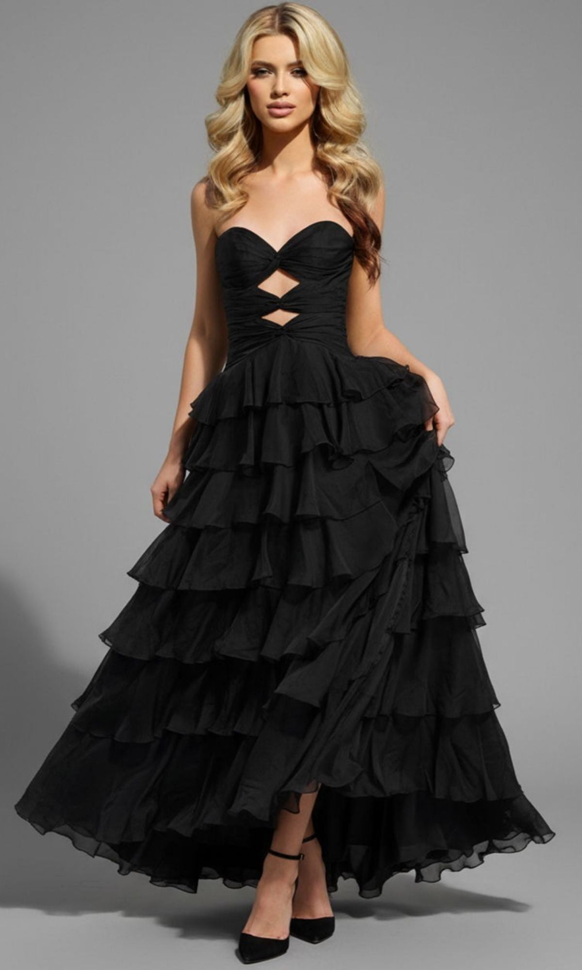 A woman models the Jovani 47743 long prom dress, featuring a strapless sweetheart neckline, cutout details, and a ruffle A-line skirt, posed against a plain gray background.